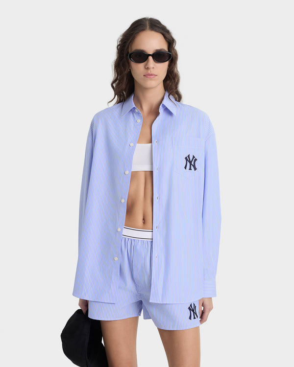 Woman wearing a light blue shirt and shorts with a logo, standing against a white background