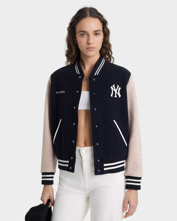 Person wearing a black and beige varsity jacket with a logo on a white background