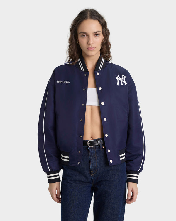 Person wearing a navy blue varsity jacket with a logo on a white background