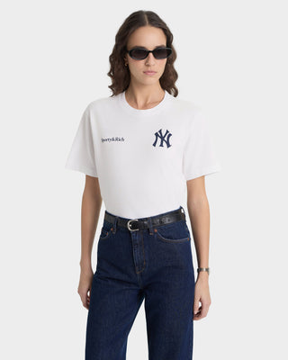 Person wearing a white t-shirt with a logo and dark jeans on a white background