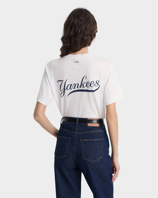 Person wearing a white t-shirt with 'Yankees' text and dark jeans on a white background