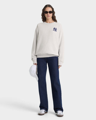 Person wearing a light gray sweatshirt with a logo and dark blue jeans on a white background