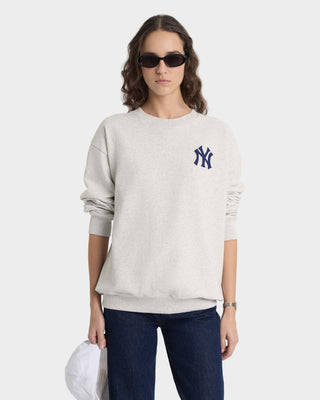 Person wearing a light gray sweatshirt with a logo, dark sunglasses, and blue jeans on a white background