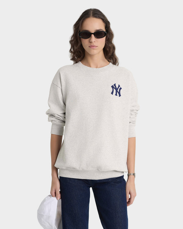 Person wearing a light gray sweatshirt with a logo, dark sunglasses, and blue jeans on a white background