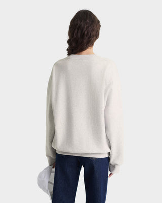 Person wearing a light gray sweater and dark blue jeans on a white background
