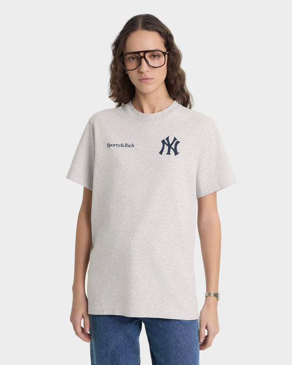 Person wearing a light gray t-shirt with 'Sporty & Rich' and New York Yankees logos on a white background