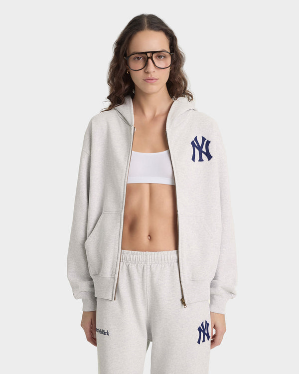 Person wearing a gray hoodie and pants with a logo, standing against a white background
