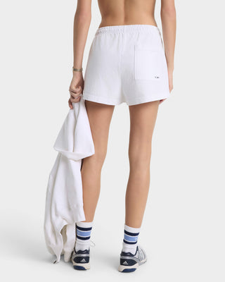 Person wearing white athletic shorts holding a towel on a plain background