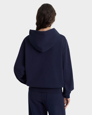 Person wearing a navy blue hoodie and pants on a light gray background