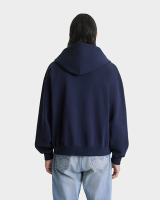 Person wearing a navy blue hoodie from behind on a light gray background