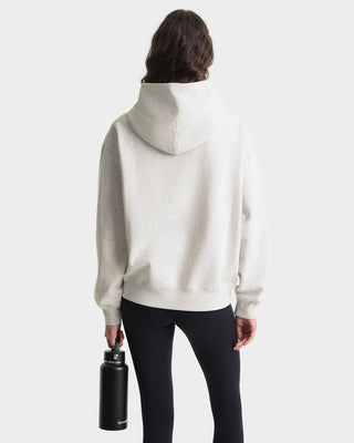 Person wearing a white hoodie holding a black water bottle on a white background