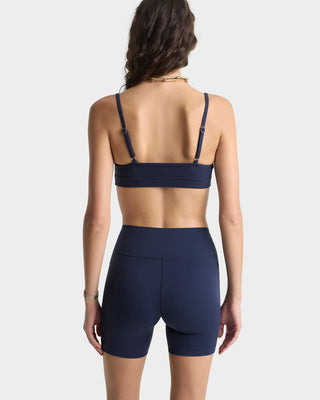 Person wearing a navy blue sports bra and shorts on a white background