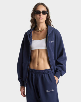 Woman wearing a navy tracksuit with 'Pretty Little' branding on a white background