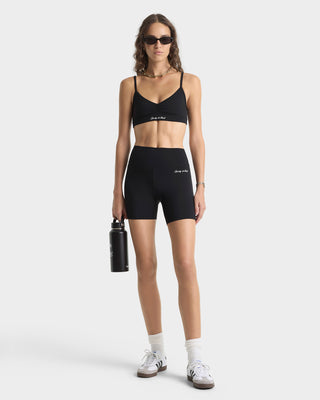 Woman wearing a black sports bra and shorts set with a water bottle on a white background