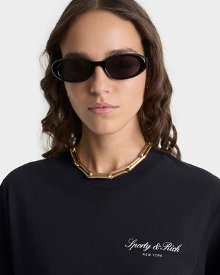 Person wearing black sunglasses and a black sweater with 'Givency & Rich' branding.