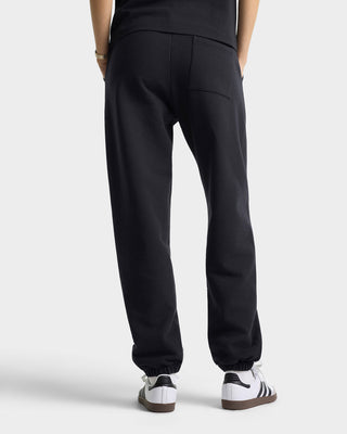 Person wearing black sweatpants with white sneakers on a light gray background