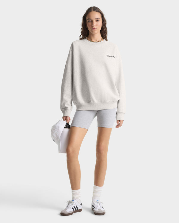 Person wearing a light gray sweatshirt and shorts holding a white cap on a white background