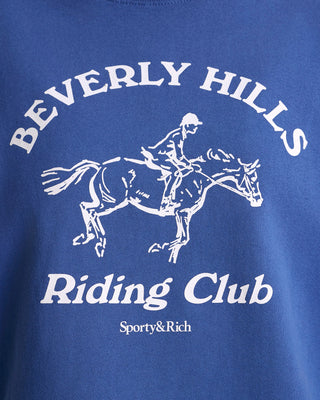 Blue t-shirt with white graphic of a rider on a horse and text 'Beverly Hills Riding Club' on a blue background.