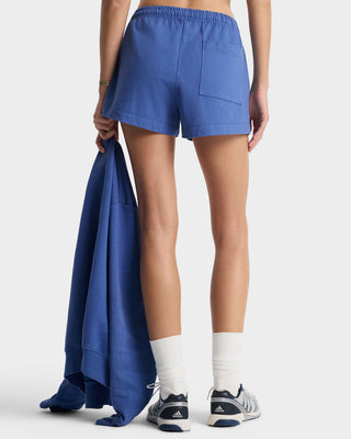 Person wearing blue shorts holding a matching blue jacket on a white background