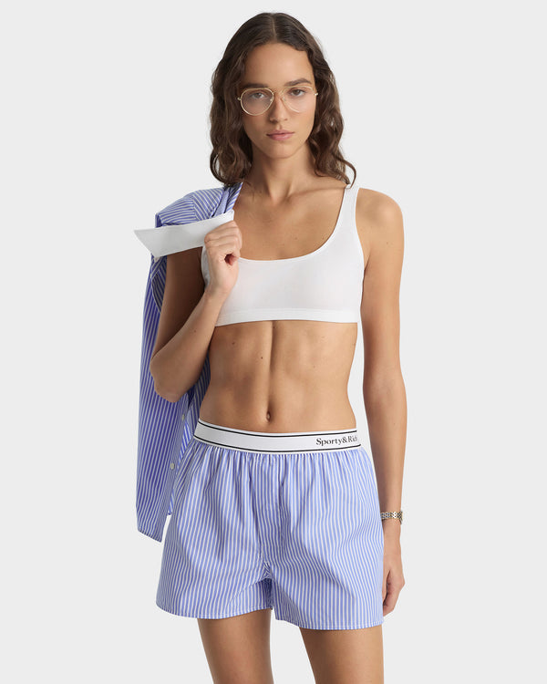 Woman wearing a white sports bra and blue striped boxer briefs on a white background