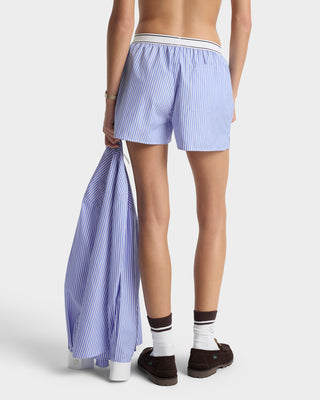 Person wearing light blue striped shorts holding a matching garment on a white background