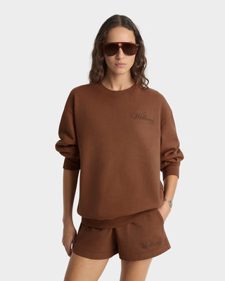 Woman wearing a brown sweatshirt and shorts set with sunglasses on a white background