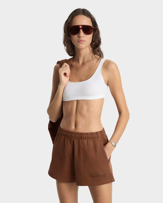 Woman wearing a white sports bra and brown shorts on a light gray background