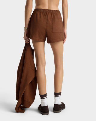 Person wearing brown shorts holding a matching garment on a plain background