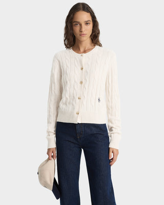 Woman wearing a cream cardigan and dark blue jeans on a white background