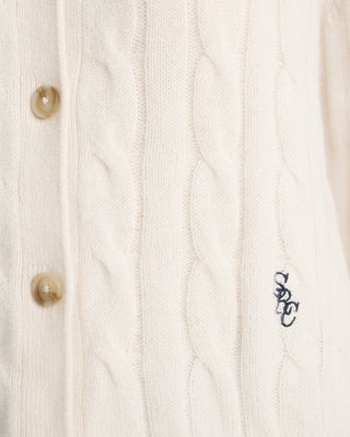 Close-up of a cable knit cardigan with button details and a brand logo.