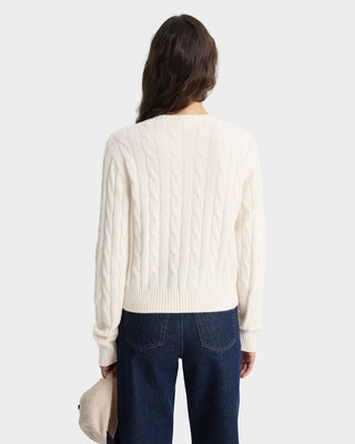Person wearing a cream cable knit sweater and dark blue jeans on a white background