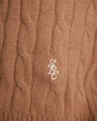Close-up of a brown cable knit sweater with a logo on it.