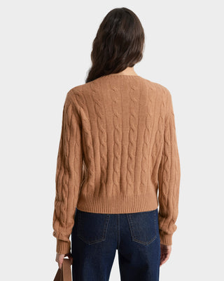 Person wearing a brown cable knit sweater and blue jeans on a white background