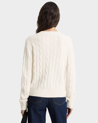Person wearing a cream cable knit sweater and dark jeans on a white background