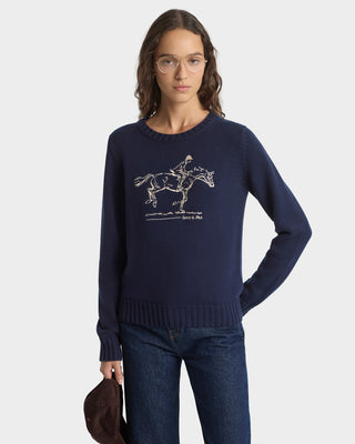 Woman wearing a navy sweater with a horse and rider design on a white background