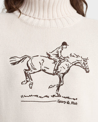 White sweater with a horse and rider illustration and 'Sporty & Rich' branding.
