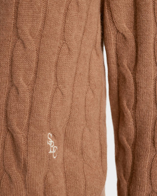Close-up of a brown cable knit sweater with a logo on a white background