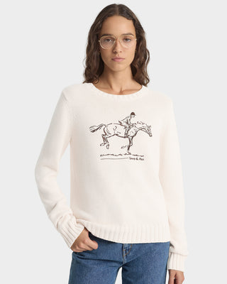 Woman wearing a white sweater with a horse and rider graphic on a plain background