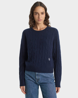 Woman wearing a navy blue cable knit sweater with a brand logo on a white background