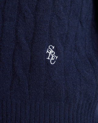 Navy blue cable knit sweater with a logo on the chest.