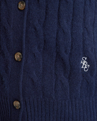 Close-up of a navy blue cable knit cardigan with buttons and a logo on the chest.