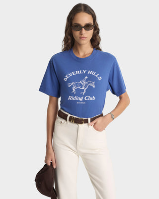 Woman wearing a blue 'Beverly Hills Riding Club' t-shirt on a white background