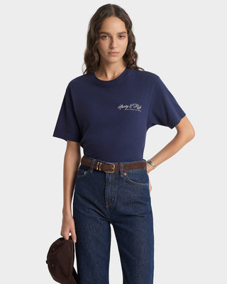 Person wearing a navy blue t-shirt with a logo and dark jeans on a white background