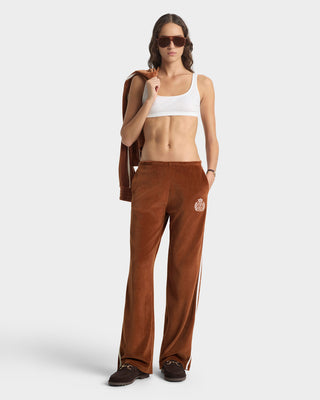 Woman wearing brown pants with a logo and a white top on a white background