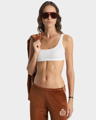 Woman wearing a white sports bra and brown pants with a brand logo on a white background