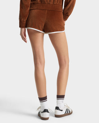 Person wearing brown shorts, white socks with black stripes, and white sneakers on a light gray background