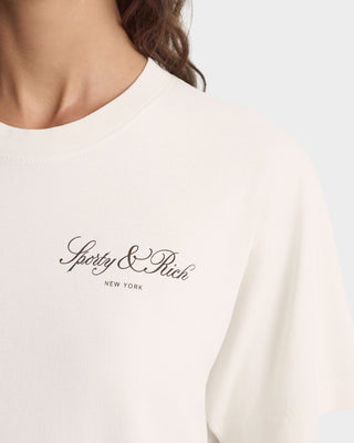 White t-shirt with 'Sporty & Rich New York' logo on a blurred background