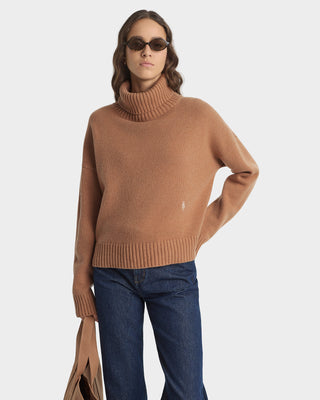 Woman wearing a brown turtleneck sweater and blue jeans on a white background