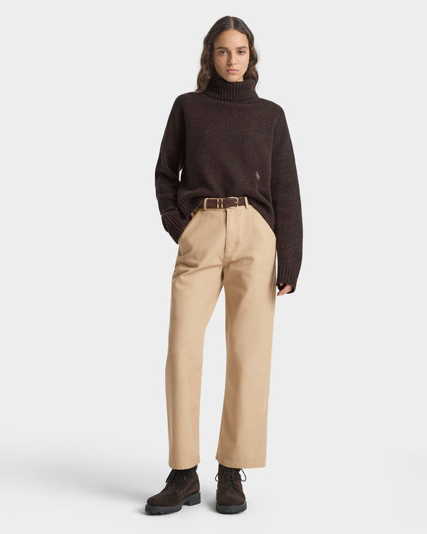 Person wearing a brown turtleneck sweater and beige pants on a white background