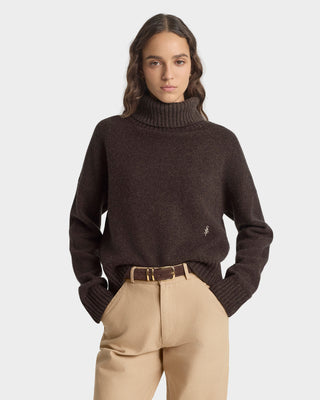 Person wearing a dark brown turtleneck sweater and beige pants on a white background